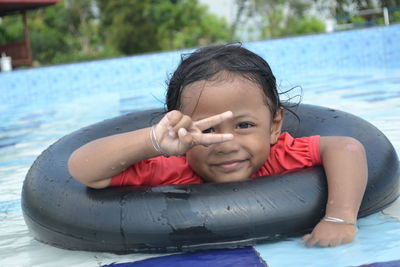 Portrait of smiling girl with inflatable ring showing peace sign while swimming in pool