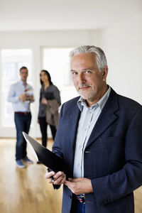 Portrait of confident male real estate agent with couple standing in background at home