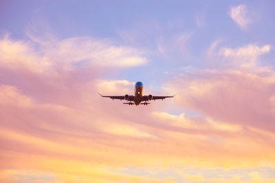 Low angle view of airplane flying against cloudy sky during sunset