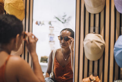 Woman trying sunglasses while looking at reflection in fashion boutique