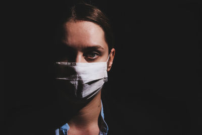 Portrait of young woman wearing mask against black background