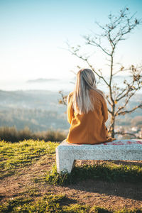 Rear view of woman sitting on field against sky