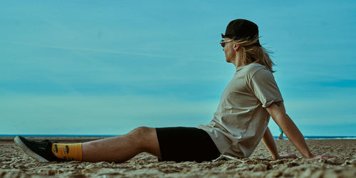 Side view of woman sitting on beach against sky