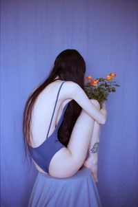 Midsection of woman holding flower standing against wall