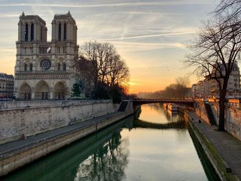 Bridge over river by building against sky during sunset