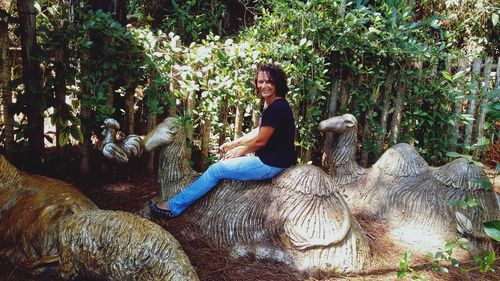 Side view of young woman sitting on tree