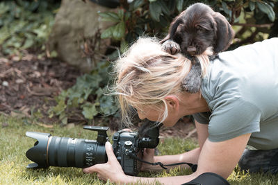 Puppy on mature woman photographing with digital camera at park