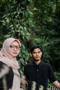 Portrait of young man with girlfriend standing on footbridge in forest