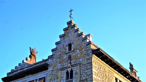 Low angle view of statue by building against clear blue sky