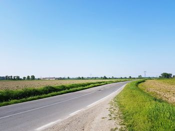 Empty road amidst field against clear sky