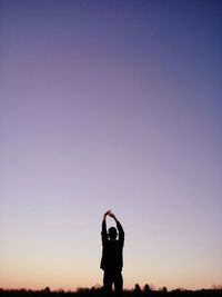 Rear view of man with arms raised standing against clear sky during sunset