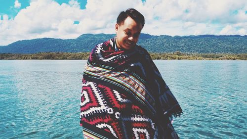 Man wrapped in blanket while standing against lake during winter