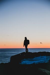 Silhouette man standing on rock at beach against sky during sunset