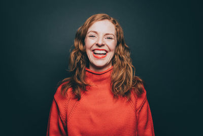 Portrait of woman in orange top laughing against gray background