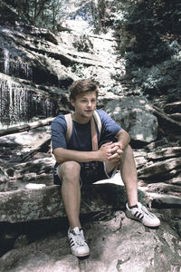 Full length portrait of young man sitting on rock