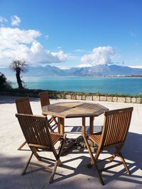 Empty chairs and table by sea against sky