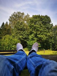 Low section of man relaxing by tree against sky