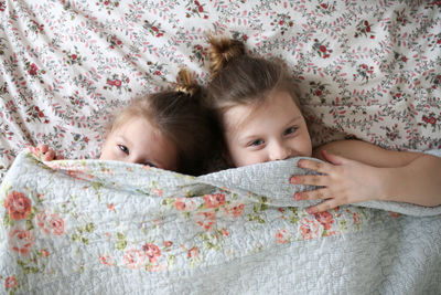 Funny children embrace, play under a blanket on the bed. concept happy childhood and siblings. 