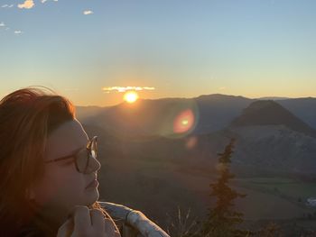 Woman looking away while wearing eyeglasses against sky during sunset