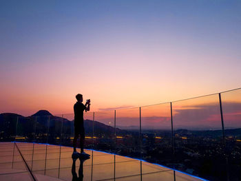 Silhouette man photographing against sky during sunset