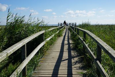 Footbridge leading towards bridge against sky