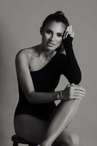 Portrait of female model sitting in bodysuit on seat against gray background