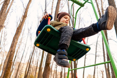 Boy sitting on swing against trees