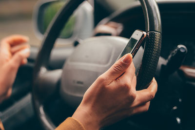 Cropped hands of woman using mobile phone while driving car