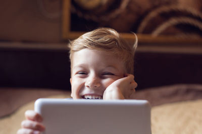 Boy using digital tablet while lying on bed at home