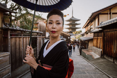 Portrait of young woman standing against building in city