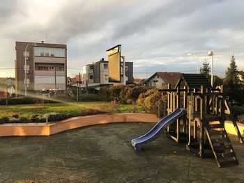 View of playground by buildings against sky during sunrise