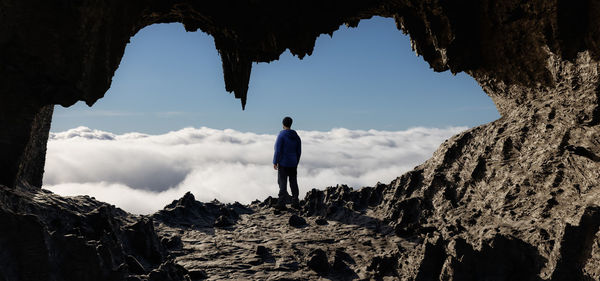 Rear view of man standing on rock against sky