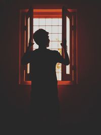 Rear view of silhouette boy standing against window at home