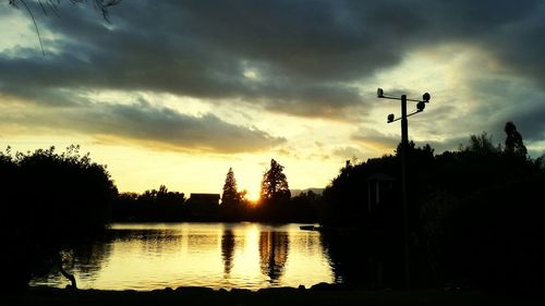 Silhouette trees by lake against sky during sunset