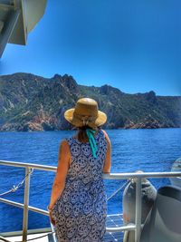 Rear view of woman standing by railing of boat on sea against clear blue sky