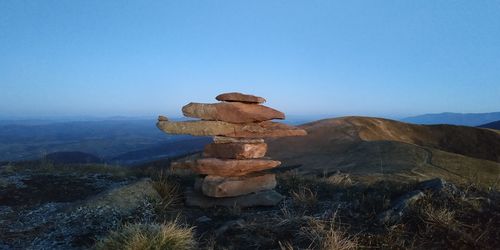 Stack of rocks on landscape against clear blue sky