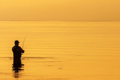 Alone fisherman standing in the sea and fishing at sunset