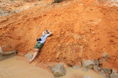 Man relaxing on rock formation by muddy river