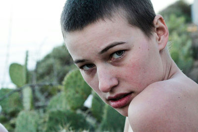 Close-up portrait of young woman against cactuses