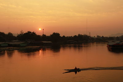 Silhouette person in river against sky during sunset