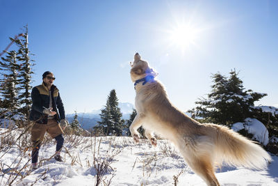 Man playing with dog on snowcapped mountain against sky