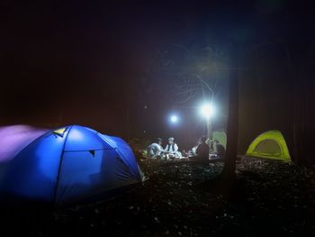 People in illuminated tent against sky at night