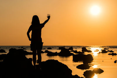 Silhouette woman gesturing while standing at beach against sky during sunset