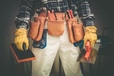 Midsection of manual worker holding work tools in workshop