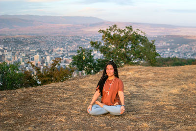 Young woman is sitting in the lotus position and meditating on mountain top.
