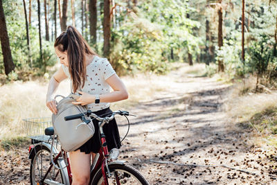 How to pack for bike ride, bicycle touring checklist. young woman with backpack riding bike in pine