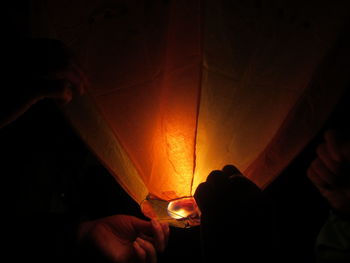 Midsection of person holding lit candle in dark