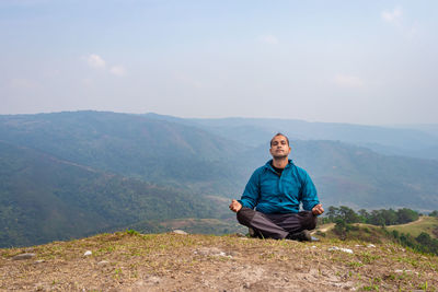 Man meditating at hill top with misty mountain rage background from flat angle