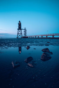 Low angle view of silhouette lighthouse by sea against blue sky during sunset