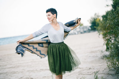 Woman holding scarf while standing at beach